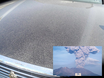 火山灰が積もったボンネットと、噴煙を上げる火山